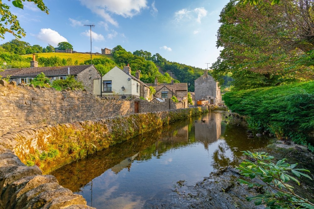 ¿Dónde alojarse en el Peak District? Los 6 mejores pueblos y buenos hoteles 10 El pueblo de Castleton y el arroyo, con las ruinas de Peveril Castle sobre las casas